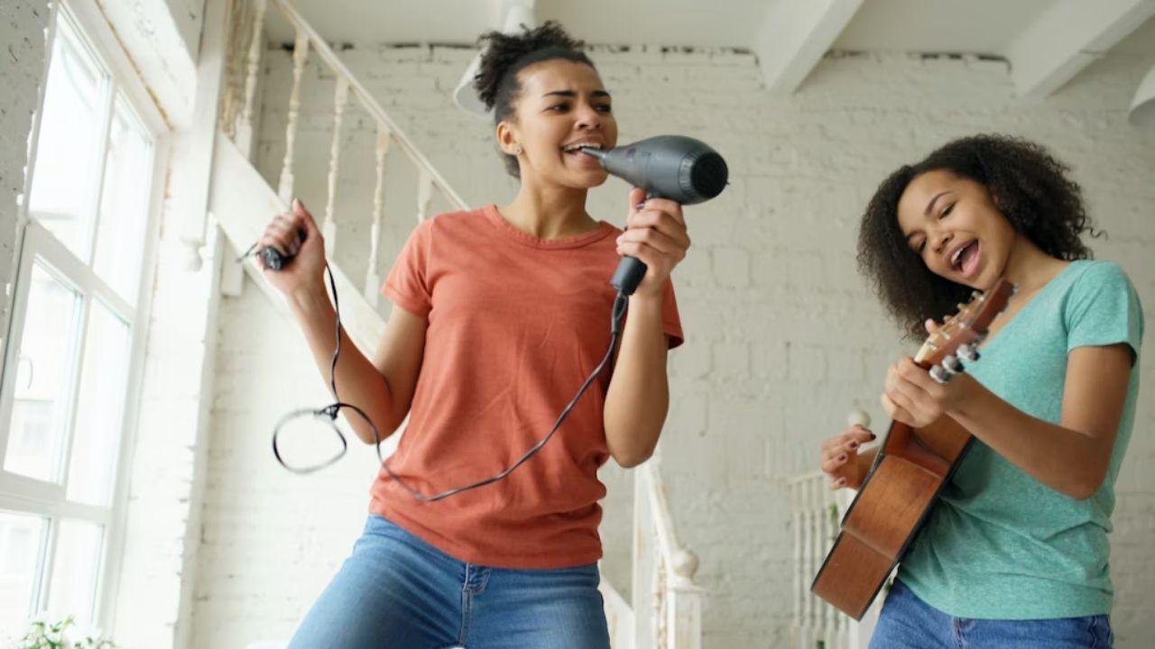 Two people singing and playing music indoors, one holding a hairdryer, build confidence as a singer.